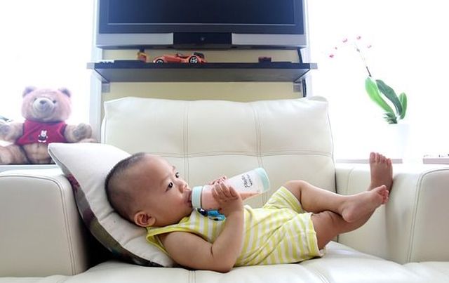 Best Baby Bottles of 2018, Baby laying on a couch drinking a pink liquid from a bottle.
