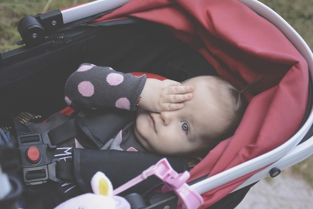 BestStrollers2019, adorable baby sitting in a pink stroller with one hand covering her eye. 