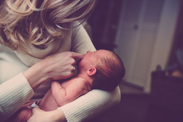Top 5 Best Nursing Bras New Moms Can't Do Without, Woman with blond hair and a white turtleneck soothing a crying newborn