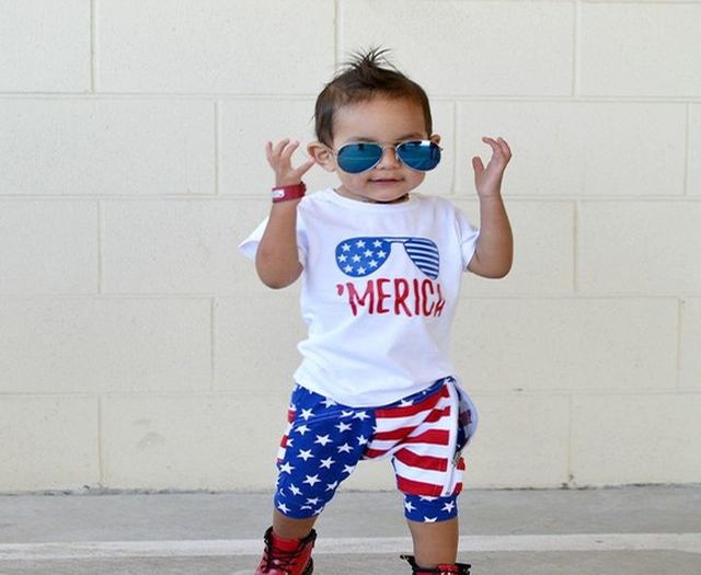 Best 2018 Baby Gifts Made in the USA, Toddler posing in American themed pants and shirt while wearing blue sunglasses and a red bracelet.