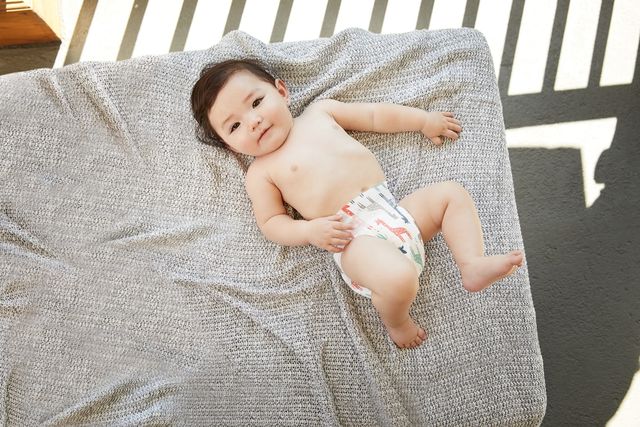 A baby lying down in a crib wearing nothing but a diaper.