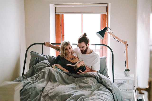 Romantic Stay-at-Home Dates (That Are Fun Too!), a couple sitting up in bed, reading a book together.