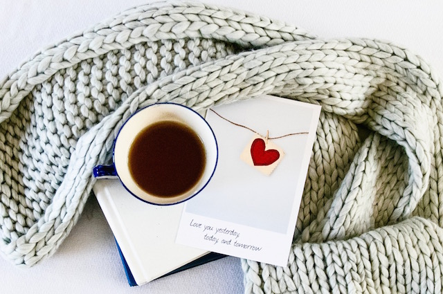 Valentine’s Day Gifts for Him, Her & Both of You, some stationary, a Valentine's Day greeting card, and a mug of coffee nested inside a knit scarf.
